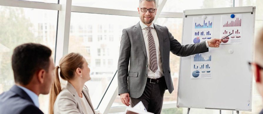 Homem mostra gráfico em reunião no escritório para dois homens e uma mulher