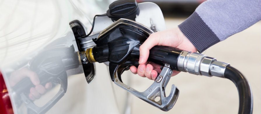 Mãos de homem abastece um carro. Ele segura um bico injetor de gasolina e parece estar em um posto de gasolina.