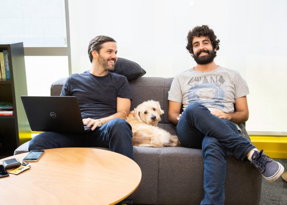 Dois homens sentados ao sofá, com um cachorro entre eles