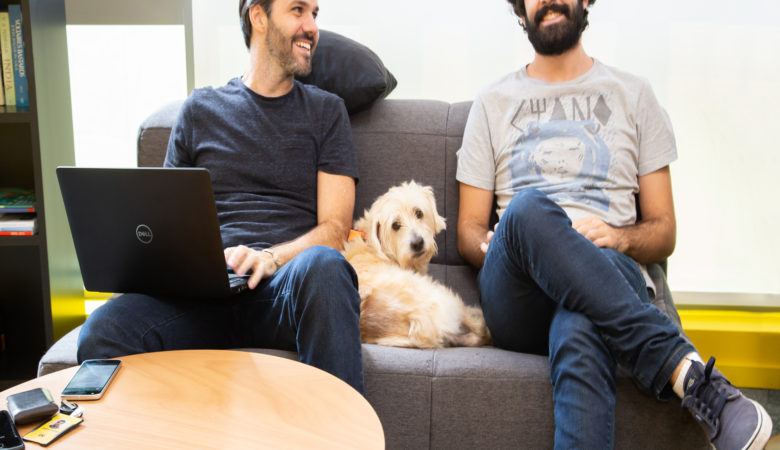 Dois homens sentados ao sofá, com um cachorro entre eles