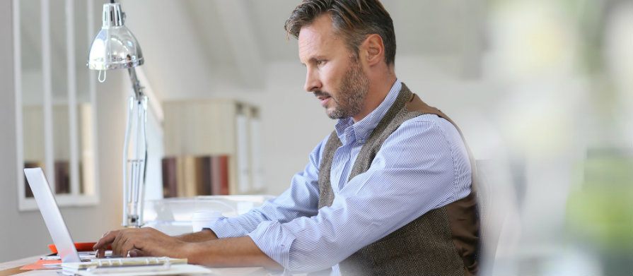 Homem vestido com roupa social usa notebook no escritório.
